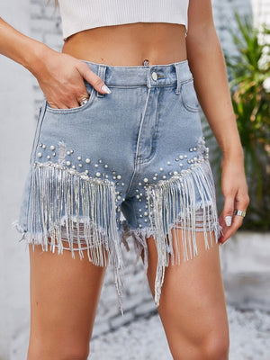 Light wash denim shorts with pearl and rhinestone embellishments and fringe detail.