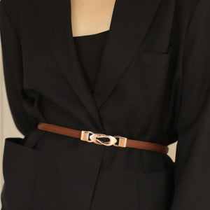 Brown leather belt with interlocking gold buckle cinching a black blazer.