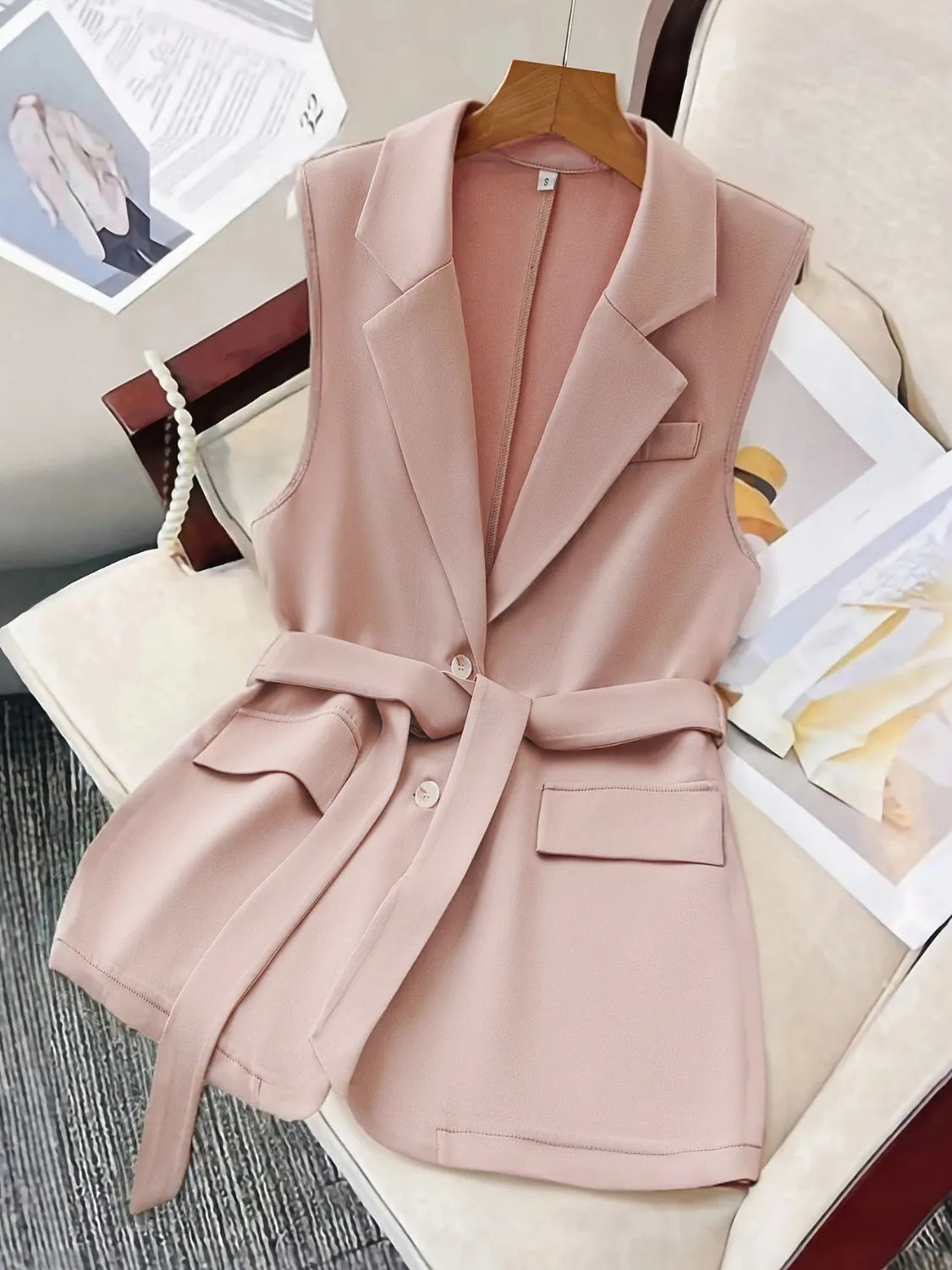 Sleeveless blush blazer with waist-defining belt and notched lapels.