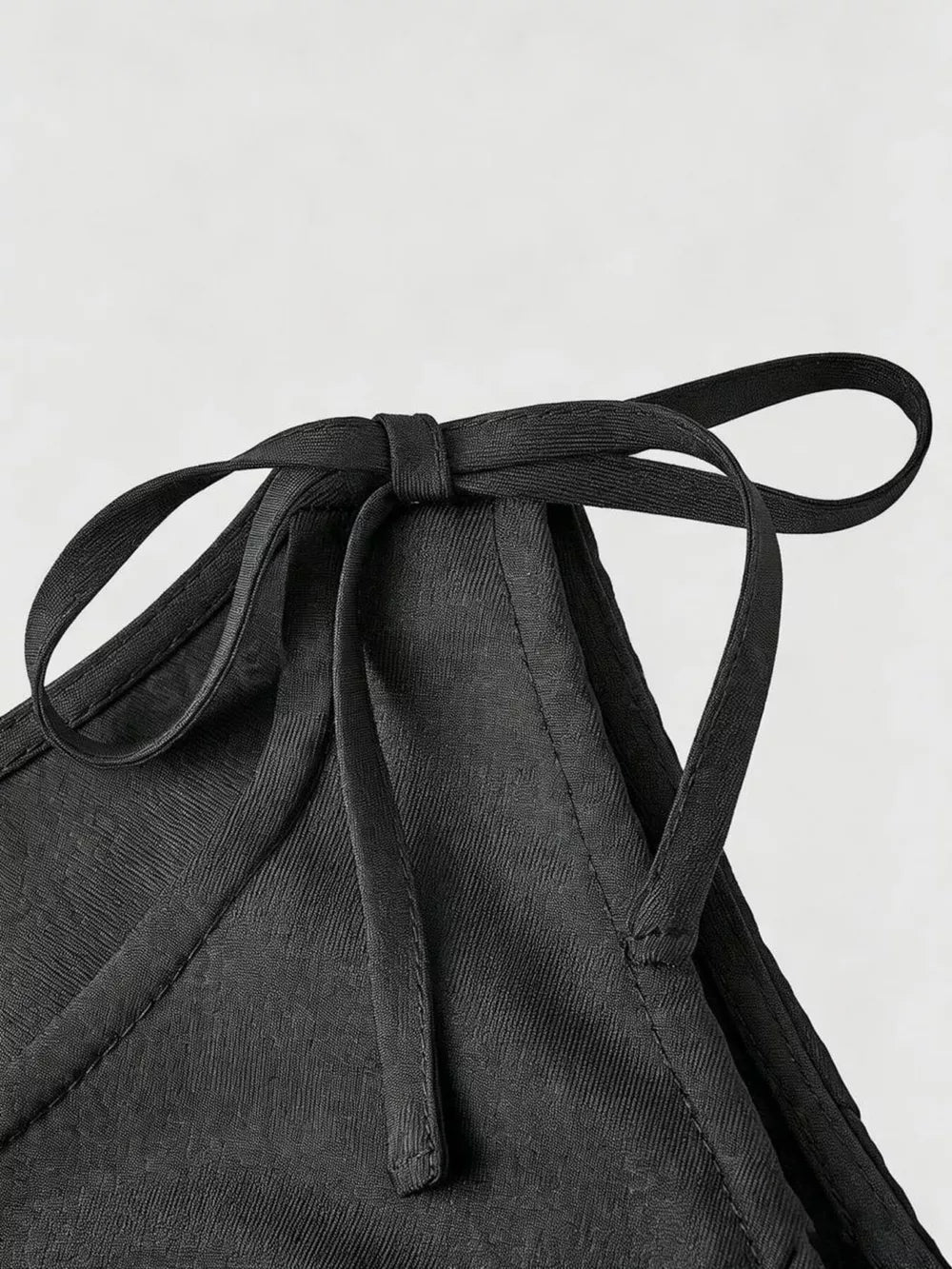 Black embellished vest with tie shoulder straps and textured fabric detail.