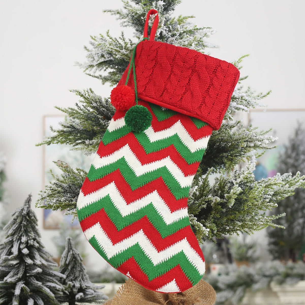 Red knit Christmas stocking with red, green, and white chevron pattern and pom-poms.