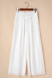 White pleated linen palazzo trousers with drawstring waist and wide leg.