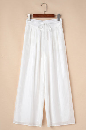 White pleated linen palazzo trousers with drawstring waist and wide leg.