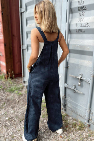 Dark blue textured wide-leg overalls with button detail and pockets.