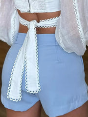 Light blue cuffed high-waisted shorts with seam detail and a white tie-back top.