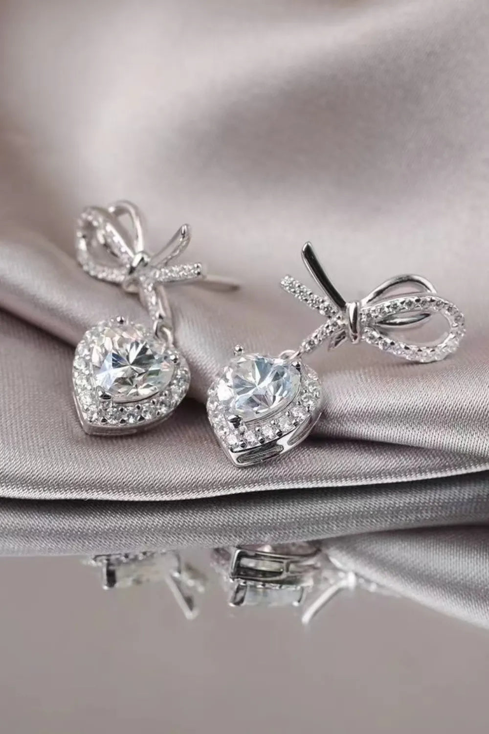 Silver bow moissanite heart drop earrings with pavé accents.