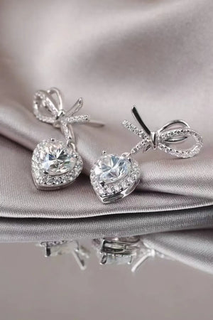 Silver bow moissanite heart drop earrings with pavé accents.
