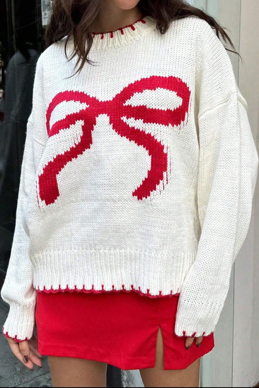 White knit crewneck sweater with a red graphic bow pattern and red scalloped trim.