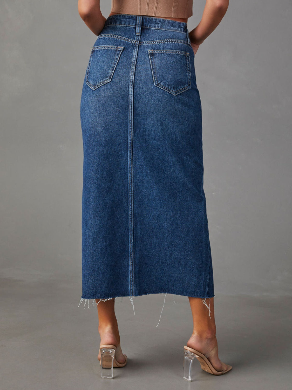 Slit-front denim midi skirt in dark blue with raw hem and buttoned closure.