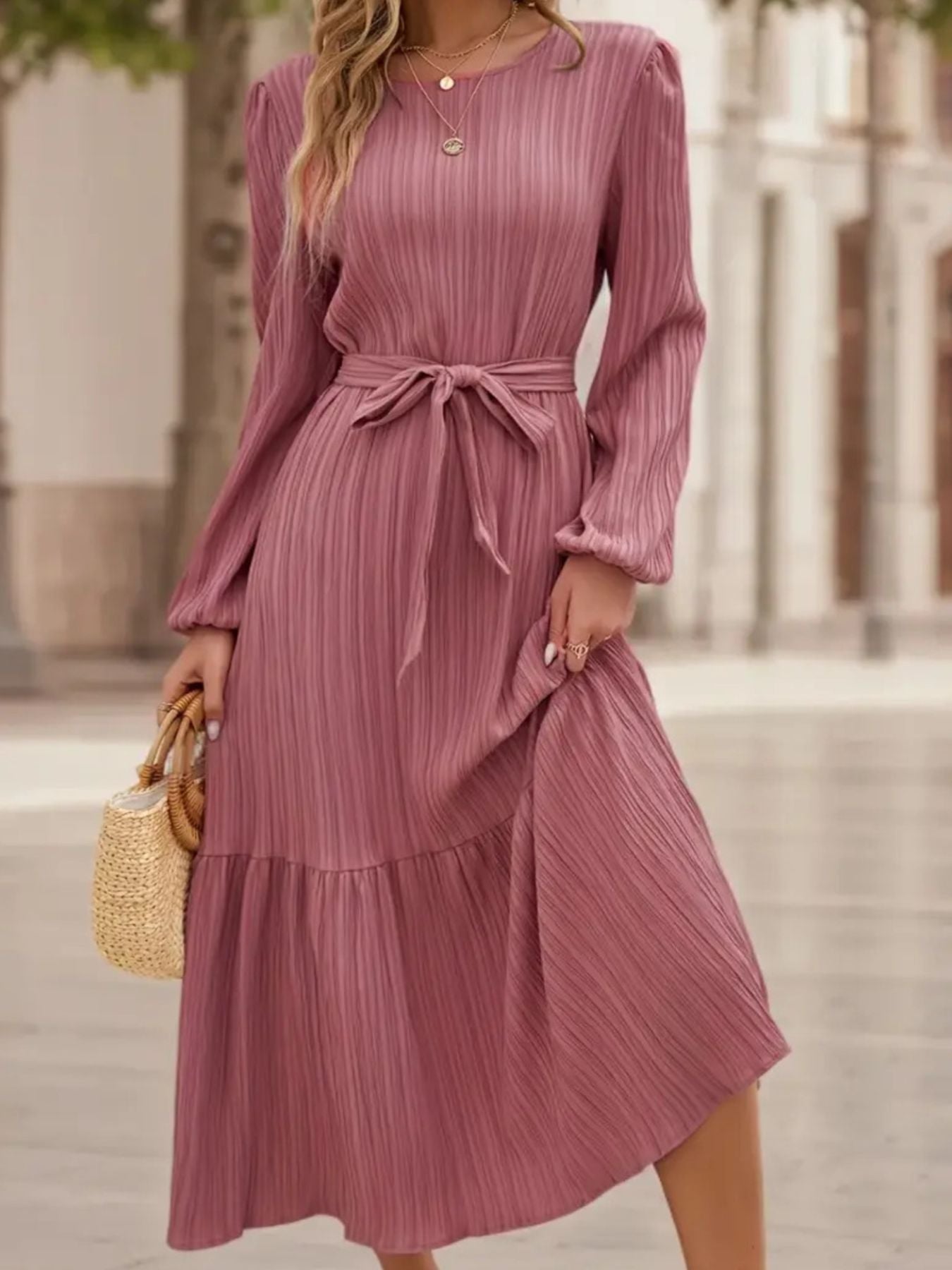 Pink pleated midi dress with long sleeves, tie waist, and tiered hem.