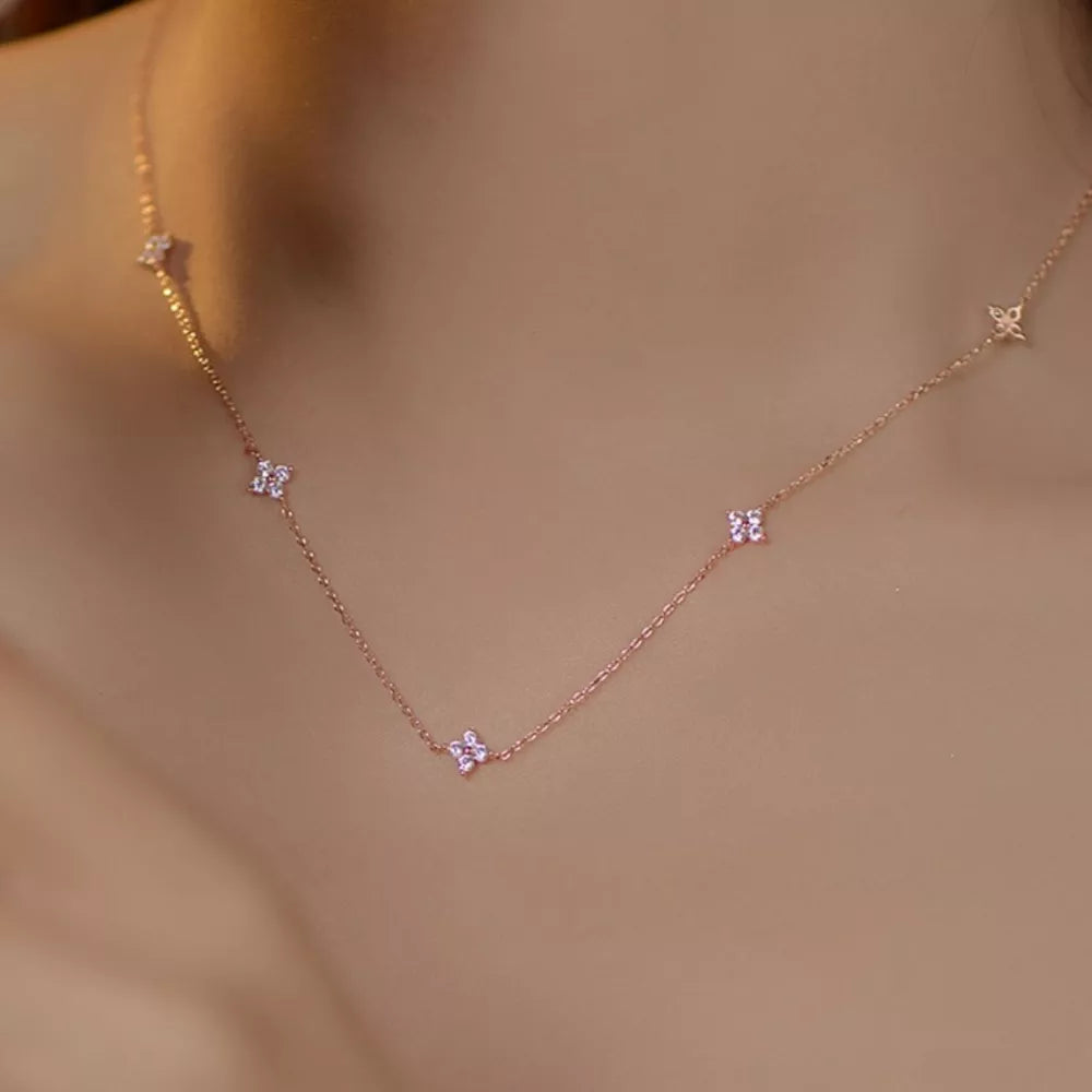 Delicate rose gold necklace with small clover charms and crystal accents.