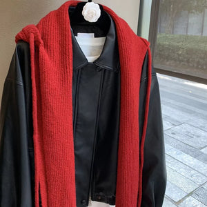 Red knit hooded scarf with tie detail draped over a black faux leather jacket.