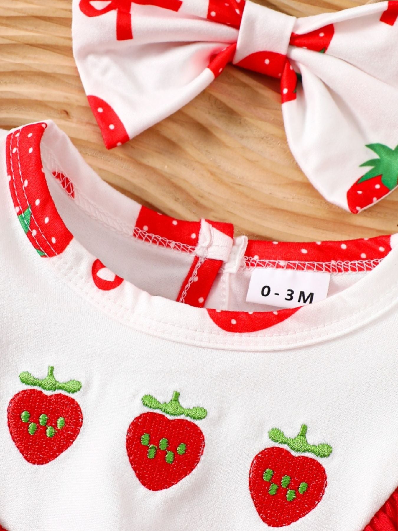 Baby one-piece set with strawberry print, red trim, and matching bow headband.