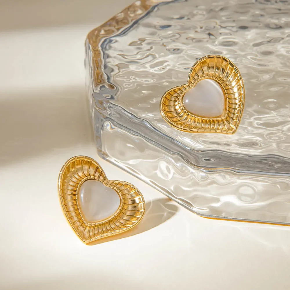 Golden heart stud earrings with ribbed details and a white cabochon center.