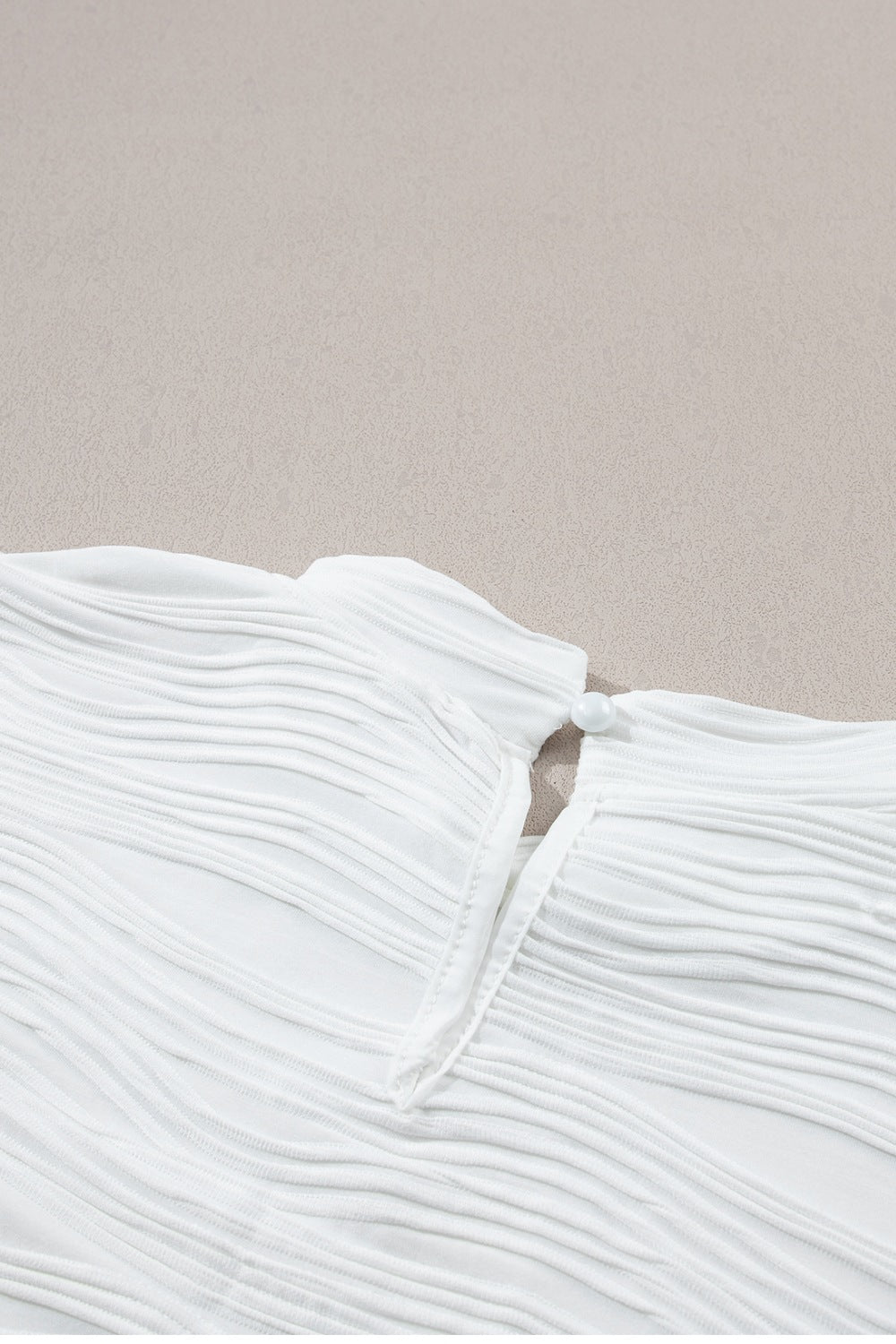 White textured cap-sleeve mock neck top with a pearl button closure at the back neck.