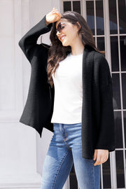 Black waffle knit cardigan with open front and relaxed fit, worn over a white top and jeans.