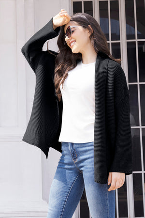 Black waffle knit cardigan with open front and relaxed fit, worn over a white top and jeans.