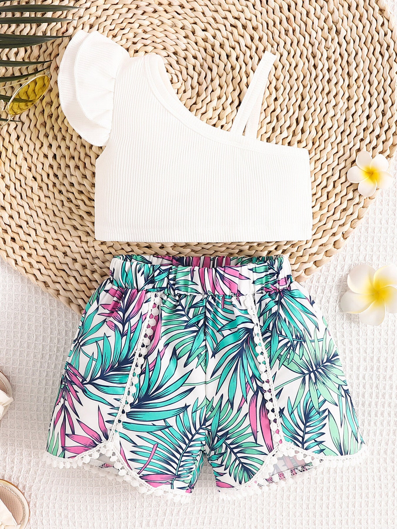 White asymmetrical top with ruffled sleeve and floral print shorts with pom-pom trim.