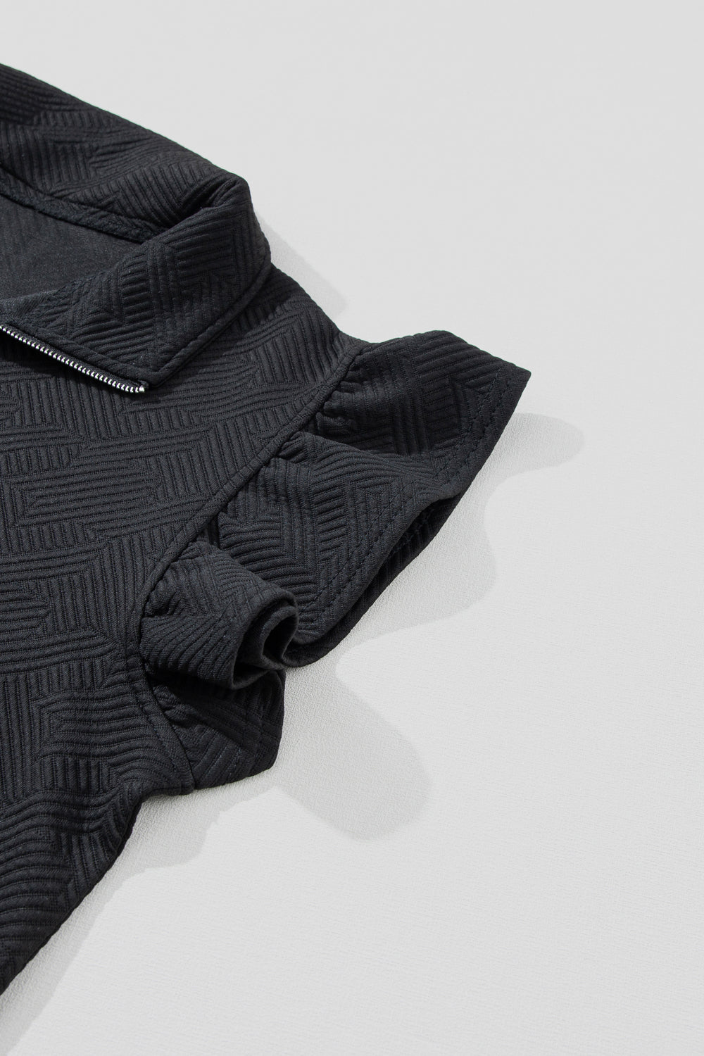 Black zip-up loungewear top with textured geometric pattern and ruffle sleeves