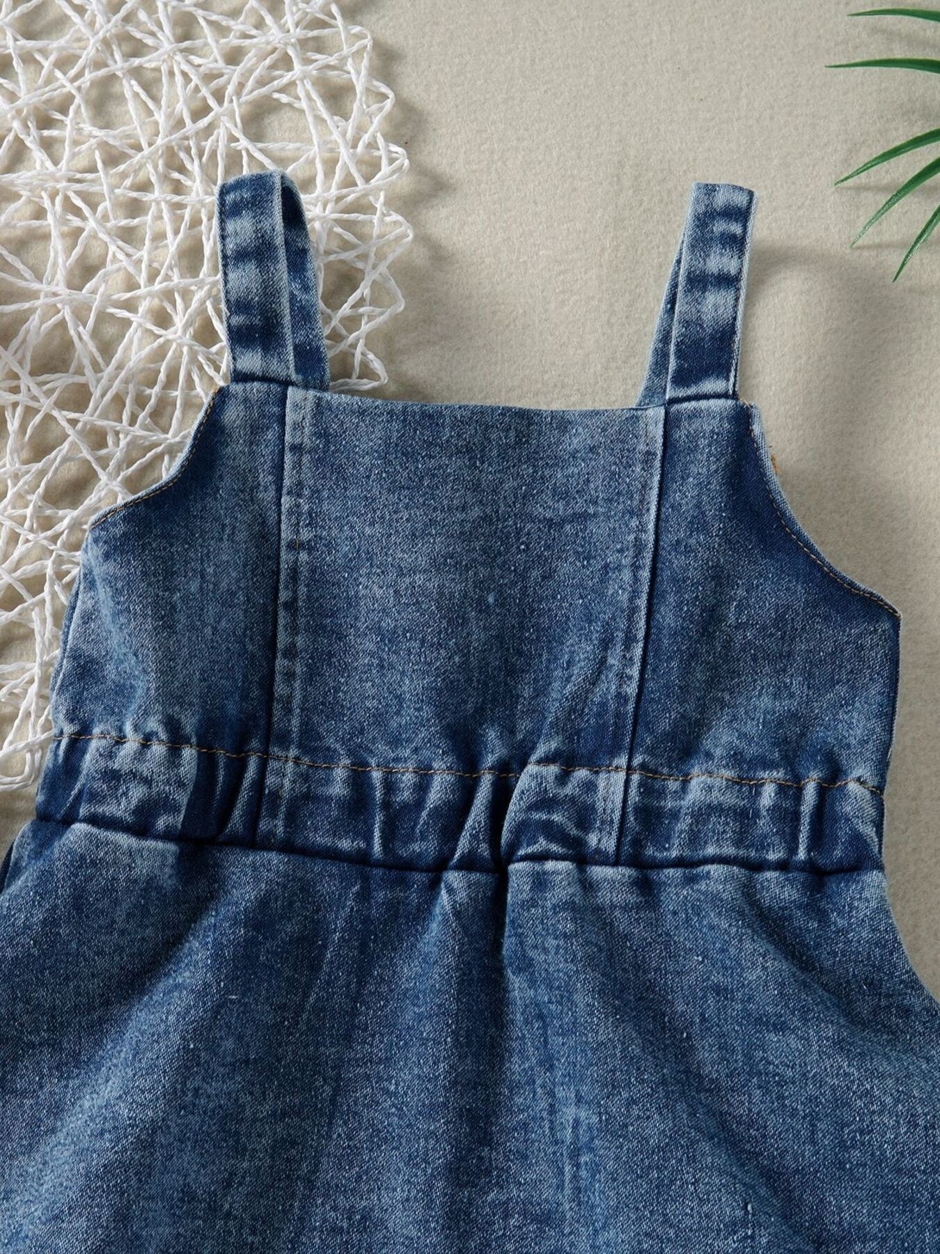 Blue denim overall dress for kids with adjustable straps and elastic waist detail.