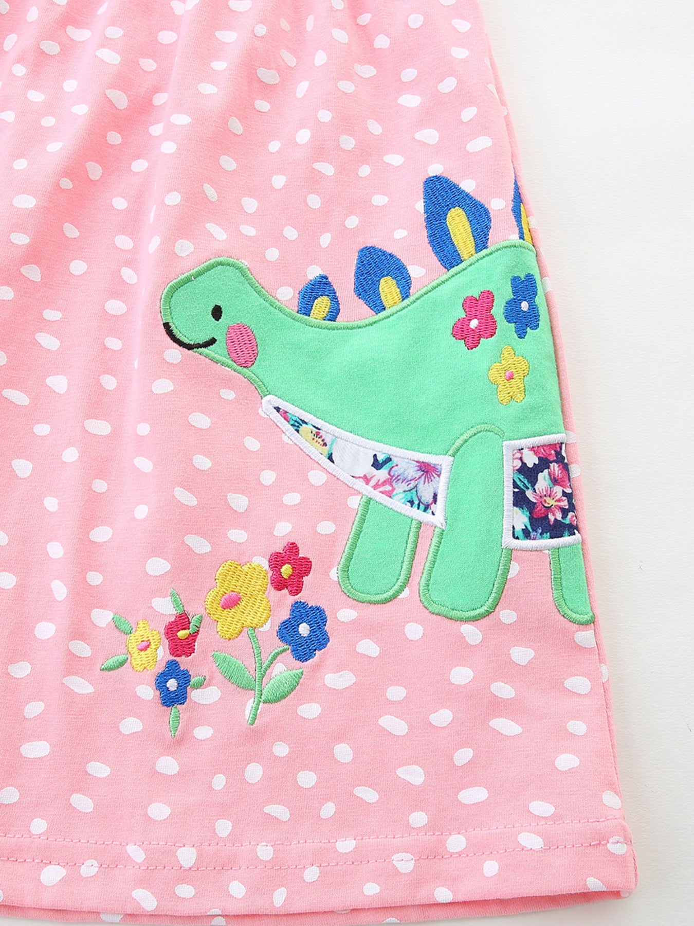 Baby dress with pink polka dots, green dinosaur appliqué, and floral accents.