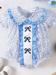 Baby one-piece with floral print, ruffle collar, and three embroidered bows on pastel blue trim.