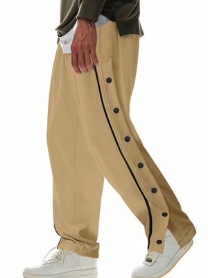 Men's khaki track pants with black snap buttons down the side and black piping.