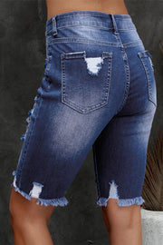 Ripped knee denim bermuda shorts in medium wash with frayed hem and distressed details.