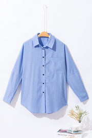 Light blue relaxed fit button-down shirt with vertical stripe texture and chest pocket.