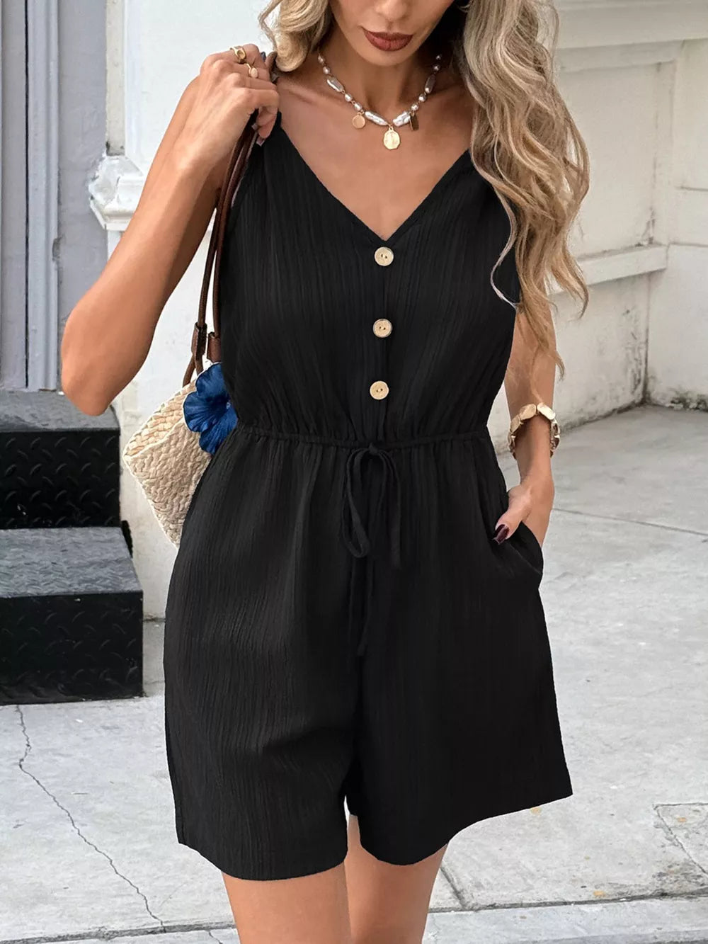 Black romper with V-neck, decorative buttons, drawstring waist, and shorts.