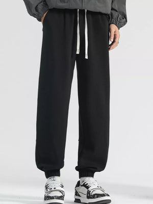 Men's black loose fit sweatpants with white drawstring and cuffed ankles.