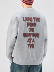 Oversized gray crew-neck sweatshirt with "Living the Dream One Nightmare at a Time" text graphic on back