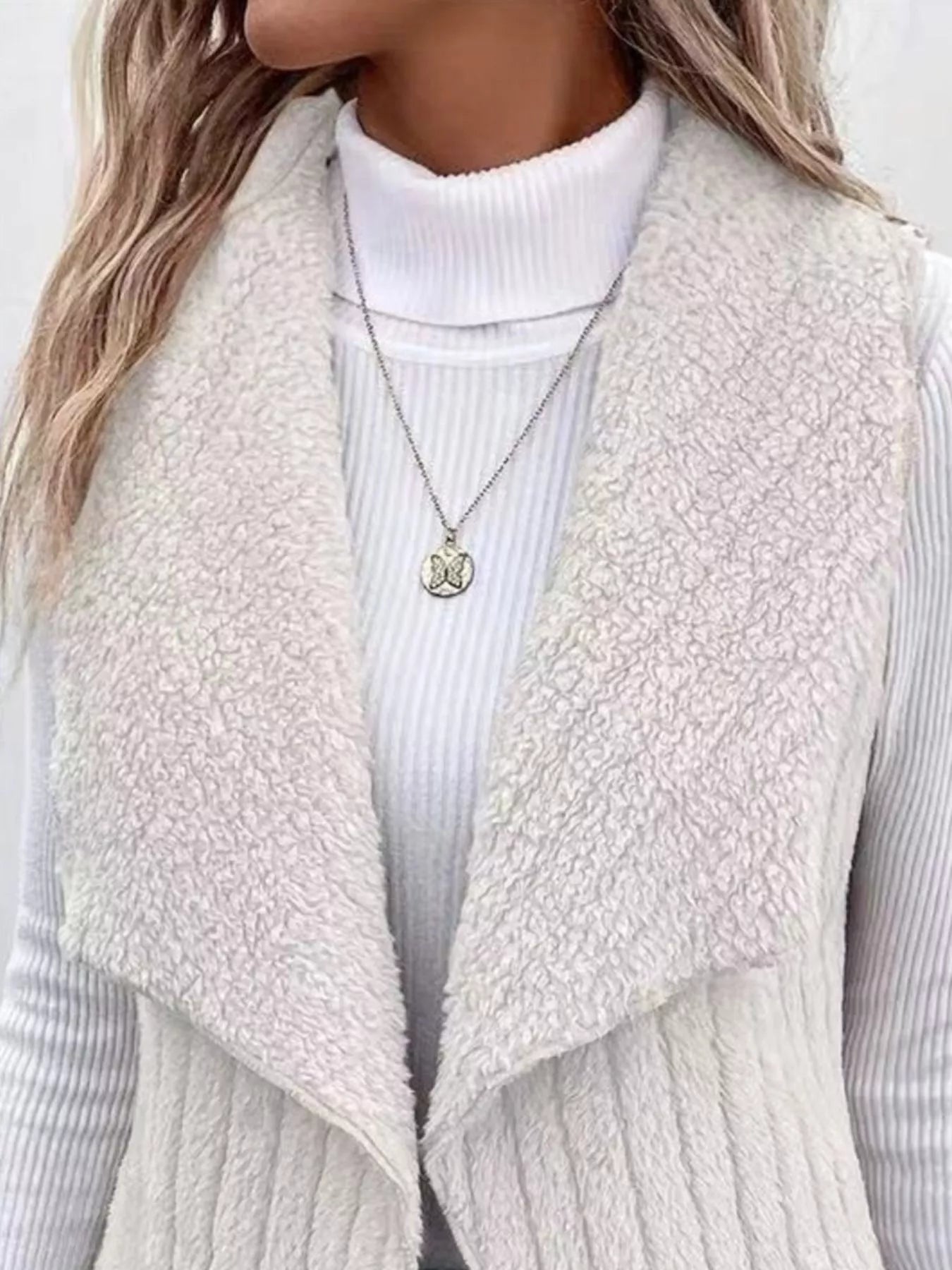 White cozy open front fleece vest with waterfall collar, worn over a turtleneck.