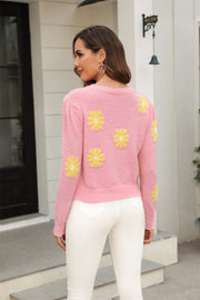 Blush pink textured knit sweater with yellow daisy motif, crew neck, long sleeves.