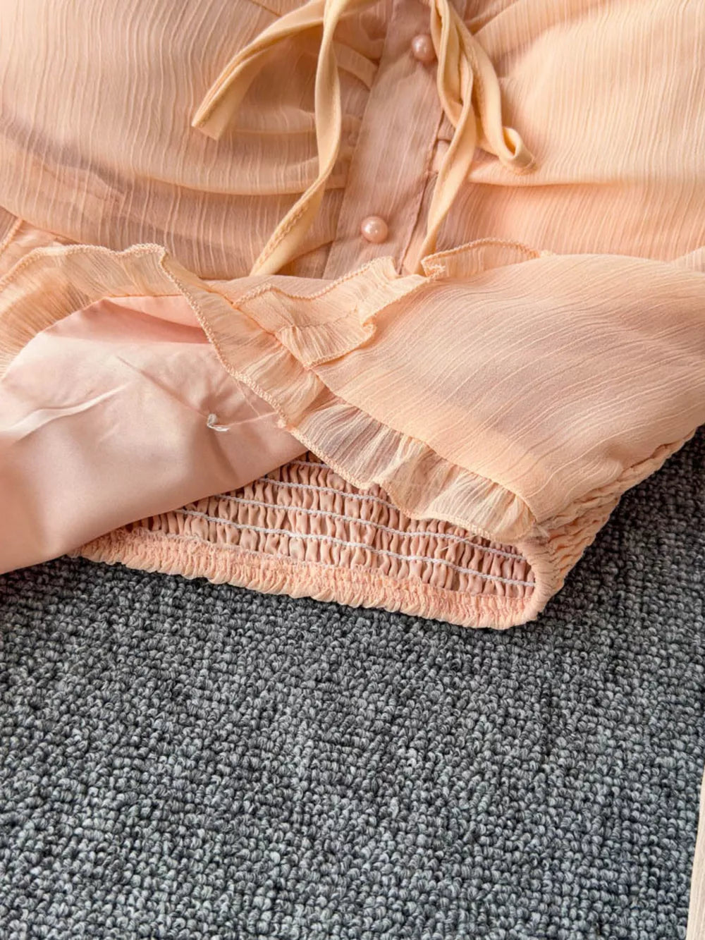 Peach maternity blouse with ruffled sleeves, tie neck, and smocked hem.