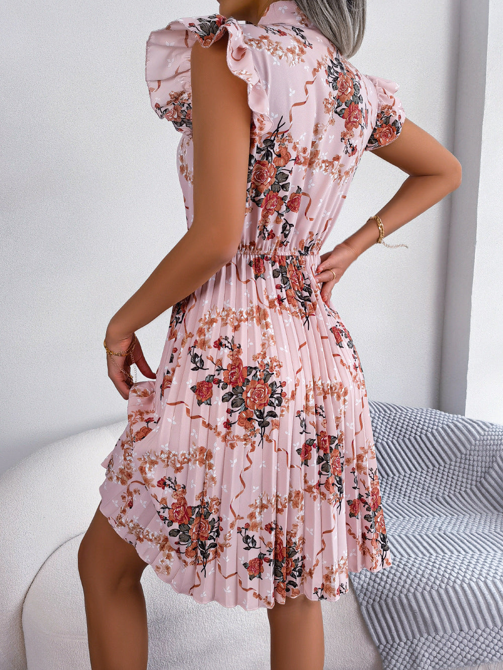 Blush pink floral mini dress with ruffled sleeves and pleated skirt.