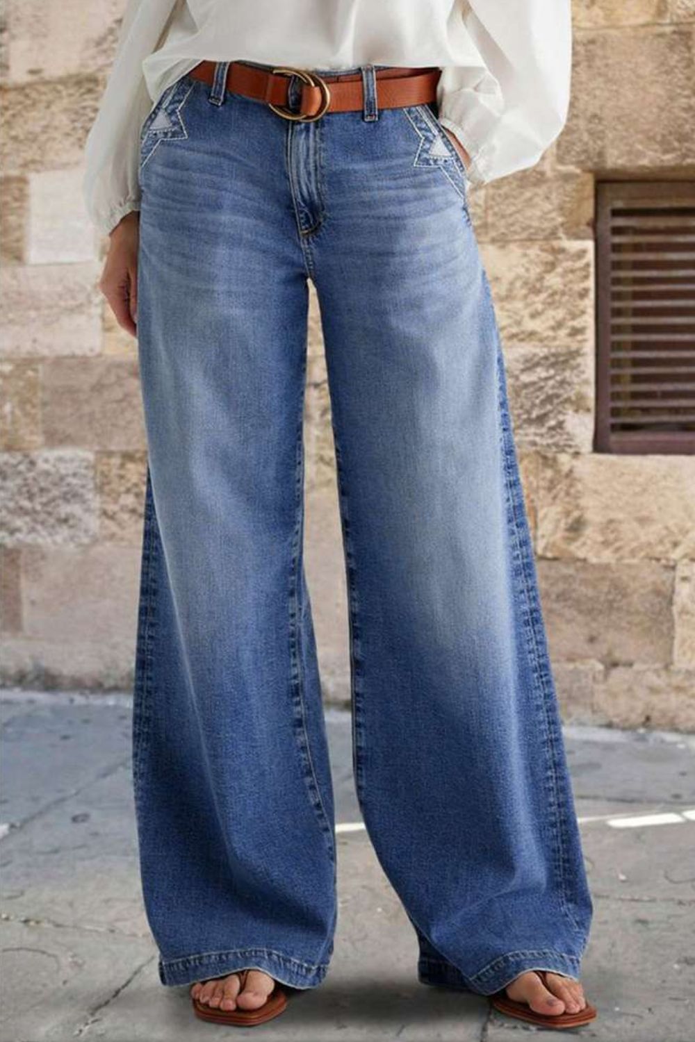 Light wash wide-leg denim jeans with subtle stitch detail on pockets and a brown belt.