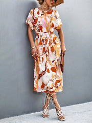 Women's abstract print midi dress in orange-red with tie waist and short sleeves.