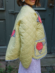 Pastel yellow quilted jacket with floral appliqué and blue striped trim.