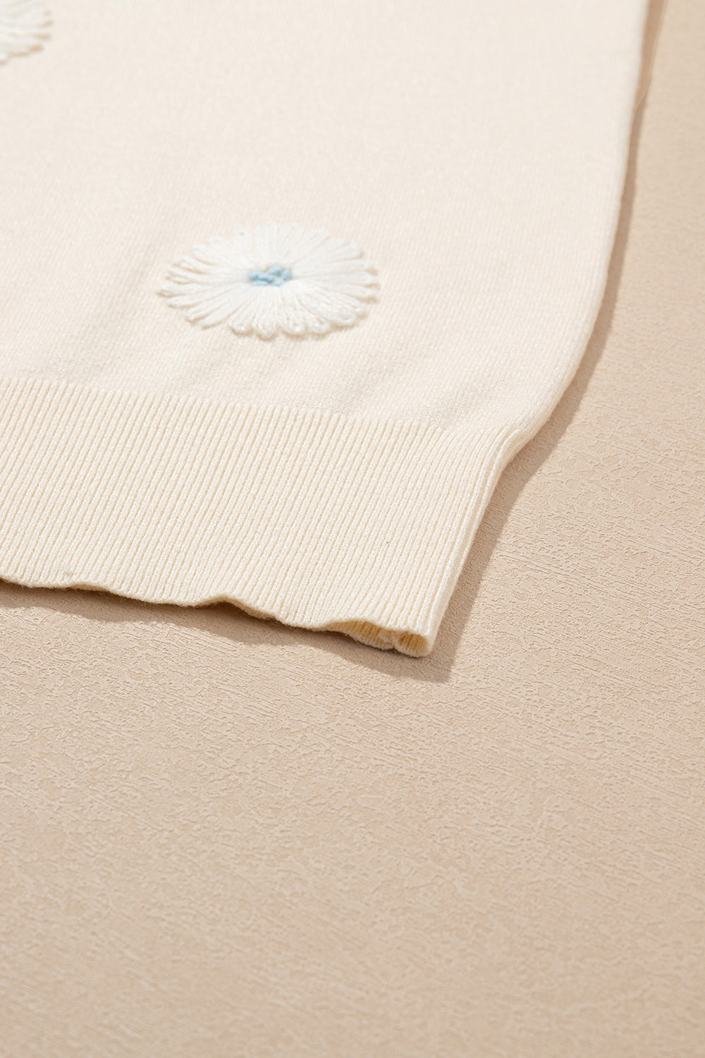 Ivory knit cardigan with white daisy appliqués and blue centers.