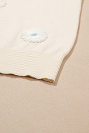 Ivory knit cardigan with white daisy appliqués and blue centers.