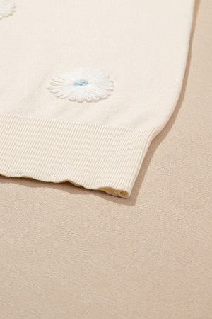 Ivory knit cardigan with white daisy appliqués and blue centers.
