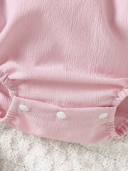 Blush pink cotton baby romper with textured fabric and white snap closure.