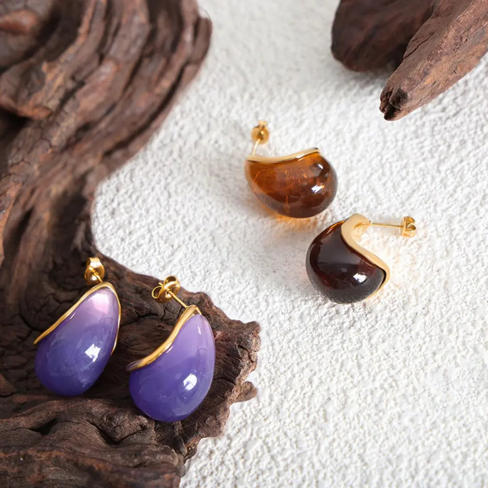 Teardrop resin stud earrings with gold trim in purple and amber tones.
