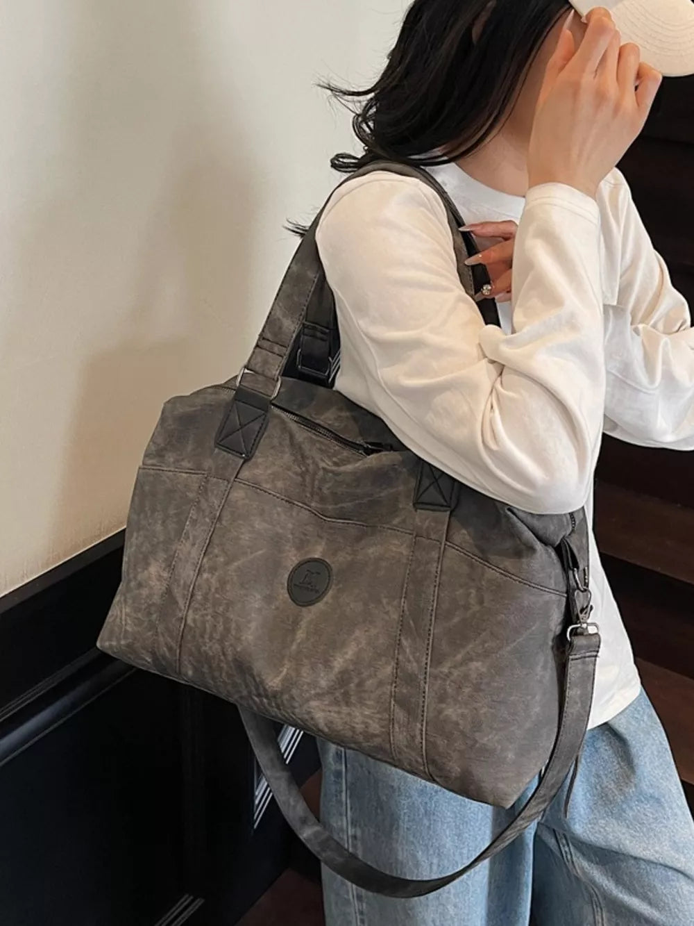Distressed dark gray leather travel duffel bag with adjustable strap and circular logo detail.