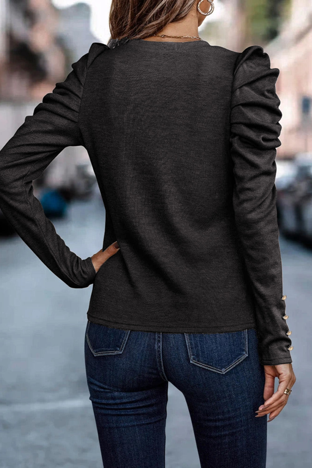 Black knit top with ruched sleeves and gold button detail on cuffs.