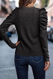 Black knit top with ruched sleeves and gold button detail on cuffs.