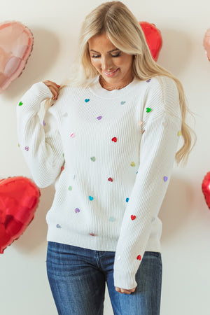 White ribbed knit sweater with scattered colorful heart embellishments.