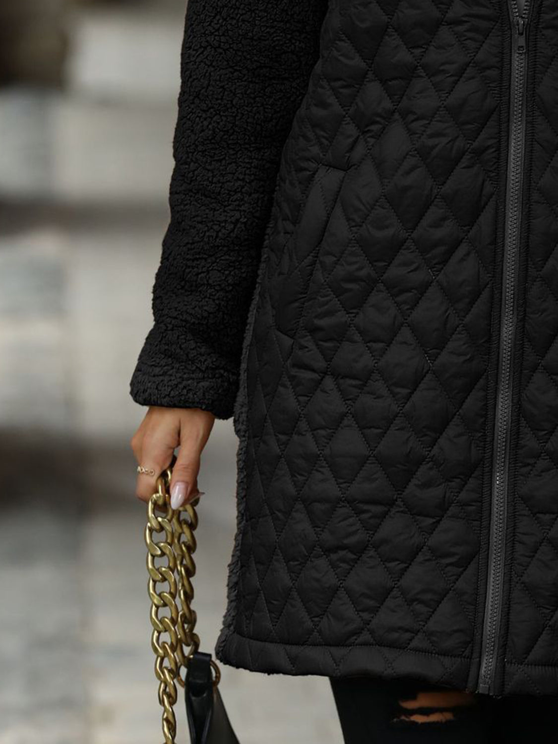 Black hybrid coat with quilted front and teddy sleeves, featuring a zip closure.
