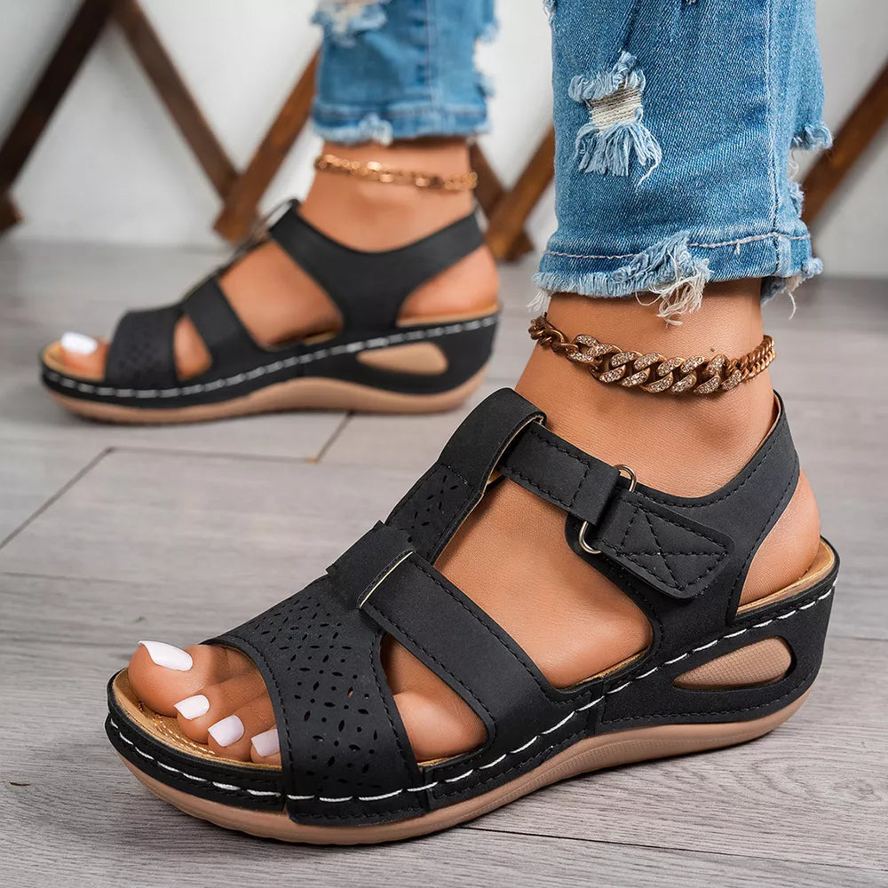 Black perforated mid-wedge sandals with adjustable straps and white stitching detail.